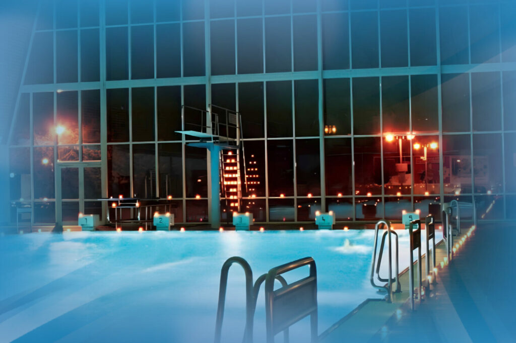 Schwimmerbecken mit Sprungturm abendlich beleuchtet